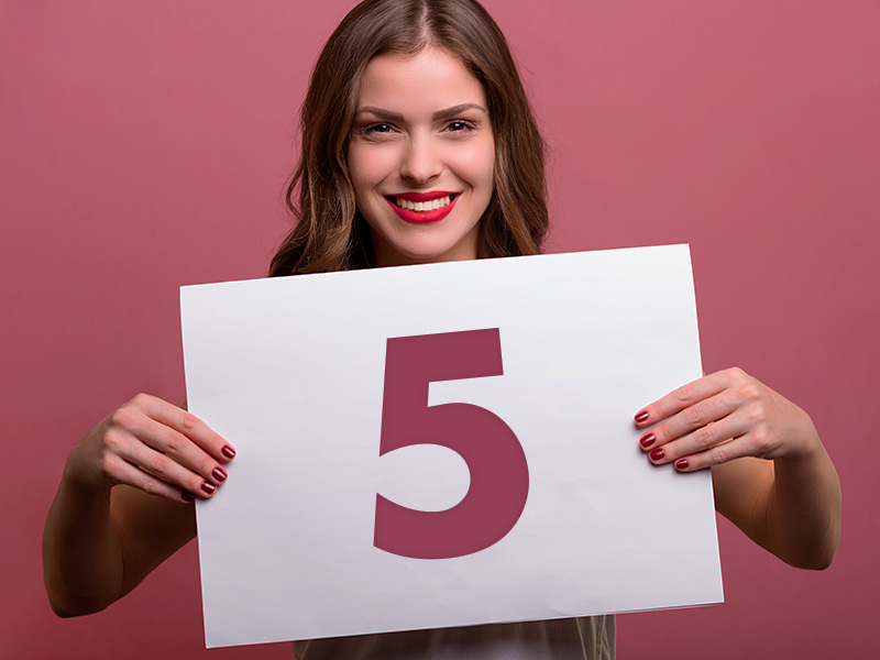 Mulher sorrindo segurando um papel com o número cinco em vermelho