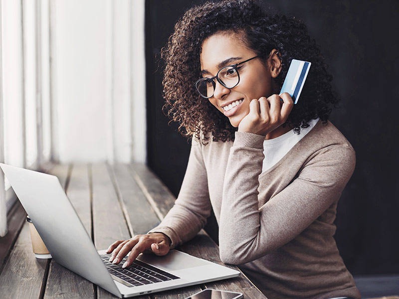 Mulher segurando um cartão de crédito para pagar o retoque da mastopexia pelo notebook