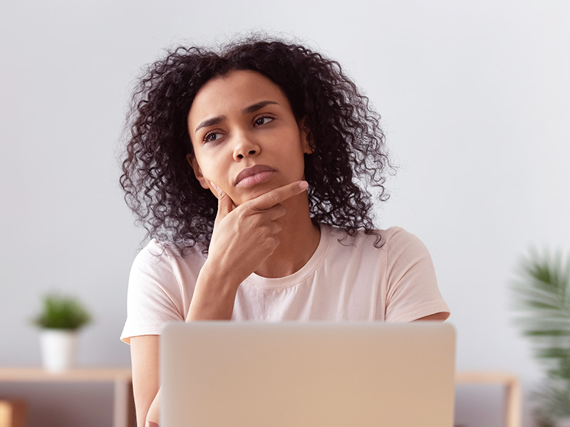 Mulher sentada na frente de um notebook com a mão no queixo pensando na diferença entre a prótese texturizada e de poliuretano