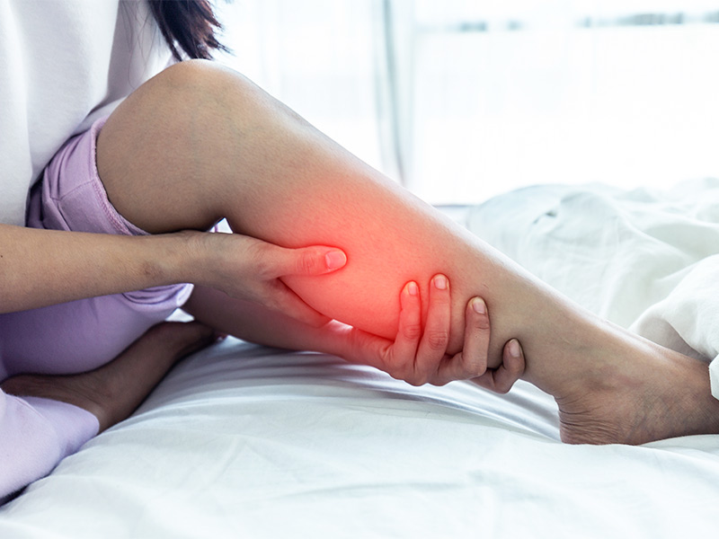 Mulher sentada na cama segurando a panturrilha porque está com dor, sinais de homans, bancroft e bandeira