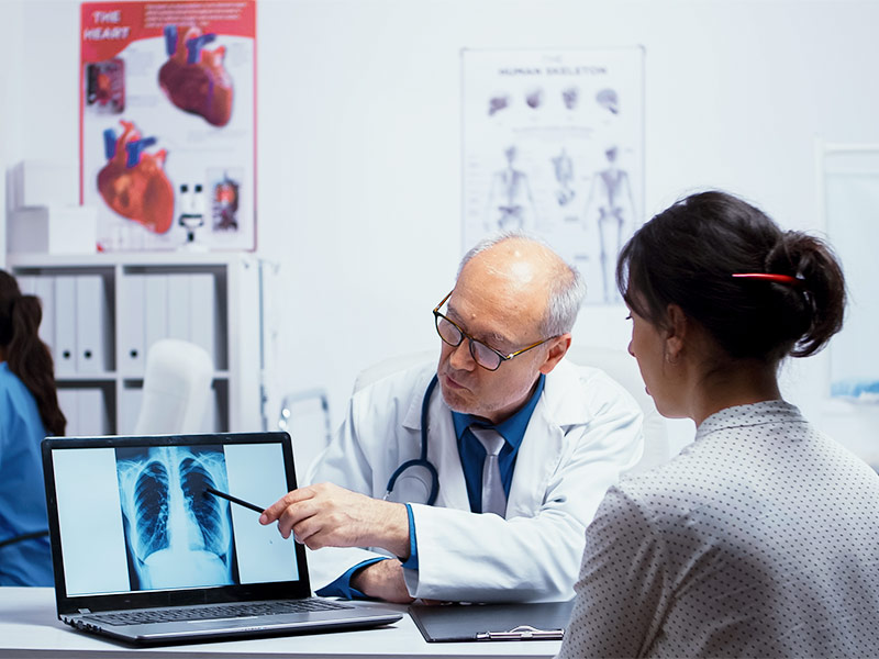 Médico apontando com lápis para uma imagem de raio x no notebook enquanto conversa com paciente