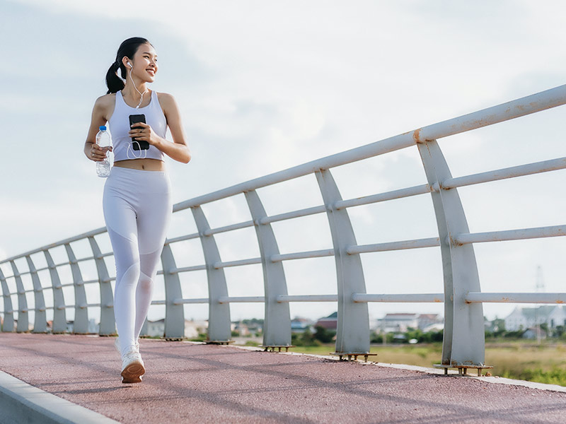 Mulher de cropped e legging branca correndo em uma ponte, em busca da cura da trombose