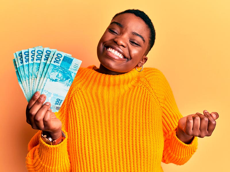 Imagem de uma mulher segurando cédulas de dinheiro e sorrindo ao saber quanto custa uma rinoplastia secundária