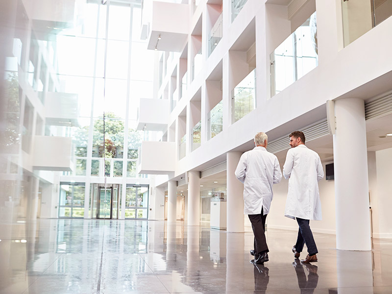 Imagem de dois médicos entrando no hospital, o lugar ideal para a realização de qualquer cirurgia plástica