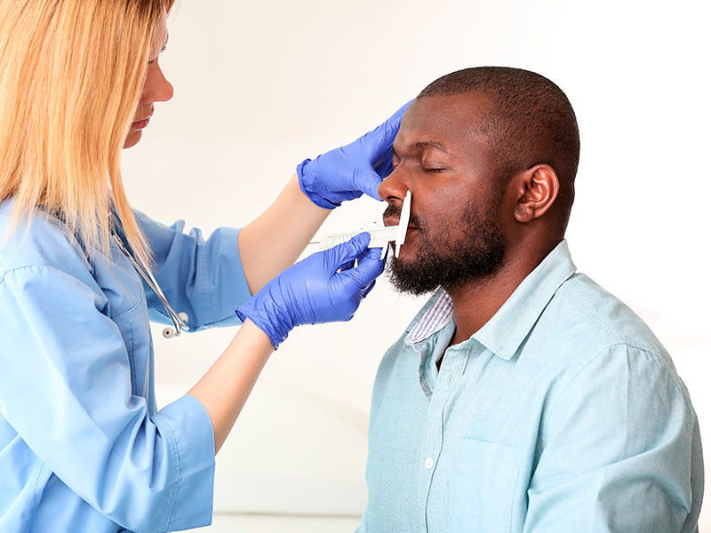 Imagem de uma cirurgiã plástica fazendo as medições do nariz do paciente antes de realizar a rinoplastia masculina 