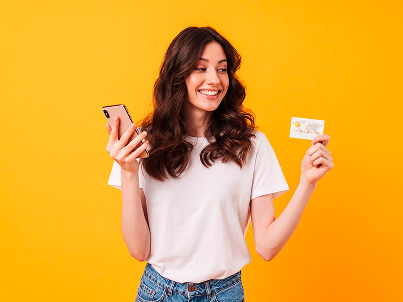 Mulher feliz segurando um celular e um cartão de crédito por causa do preço da cirurgia para fechar a orelha