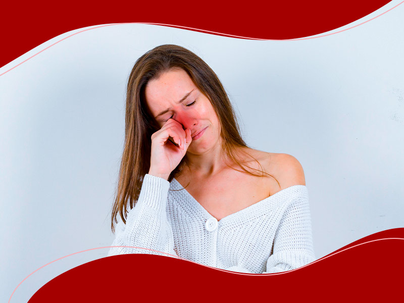 Mulher com a mão no rosto e expressão de dor, com uma bolinha vermelha na região do nariz, simbolizando um dos sintomas do desvio de septo, congestionamento nasal e dificuldade para respirar