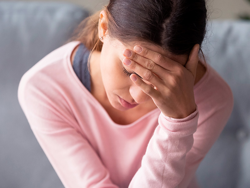 Imagem de uma mulher com a mão na testa, sentindo enxaqueca, um dos sintomas do desvio do septo