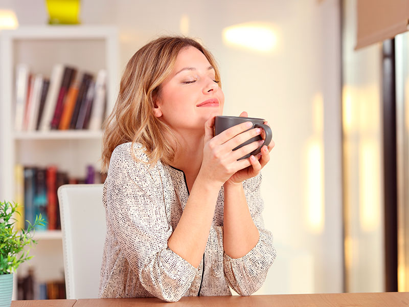 Imagem de uma mulher segurando uma xícara de chá, com expressão de felicidade por ter realizado a cirurgia no nariz