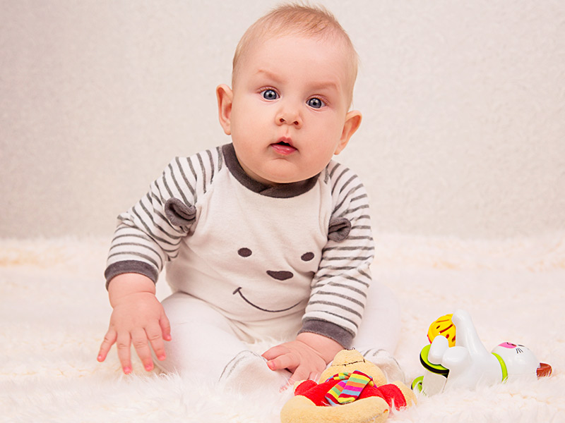 Bebê sentado com dois brinquedos, que vai usar o dispositivo corretor de orelha de abano