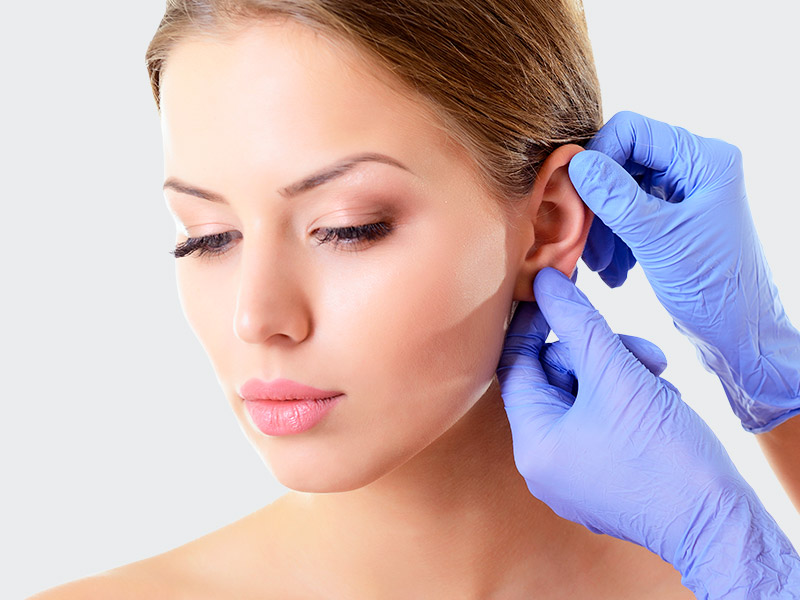 Na imagem, um profissional da saúde está analisando a orelha da paciente antes da cirurgia lobuloplastia