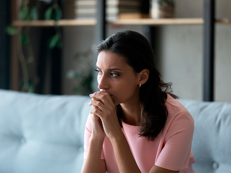 Imagem de uma mulher sentada no sofá com expressão de preocupação ao descobrir sobre as complicações dos fios de sustentação