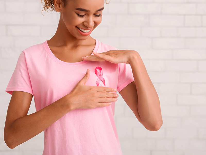Mulher de camiseta rosa e um lacinho, divulgando que o bico invertido pode ser câncer de mama
