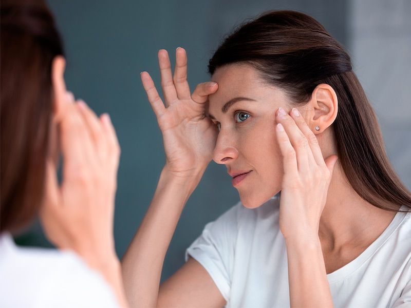 Foto de uma mulher se olhando no espelho e pensando se o ácido hialurônico mancha a pele