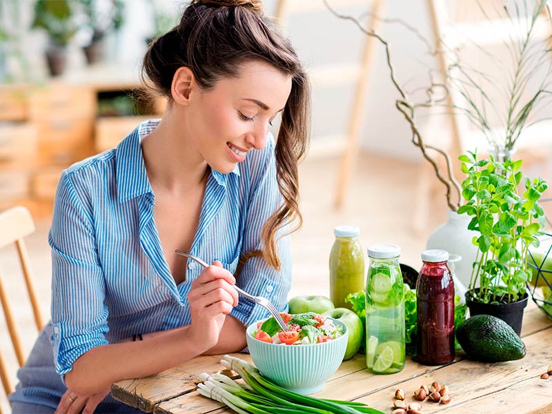Quais os principais cuidados para um ótimo antes e depois da cirurgia de abdômen? Mulher feliz comendo salada sentada em uma mesa