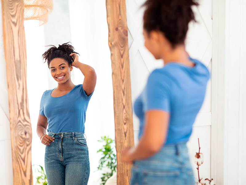 Mulher feliz admirando o antes e depois da sua cirurgia plástica no espelho