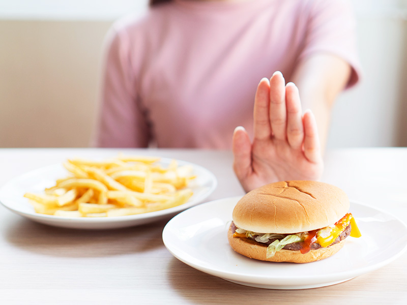 alimentos inimigos barriga chapada, na imagem uma mulher está afastando um hambúrguer 