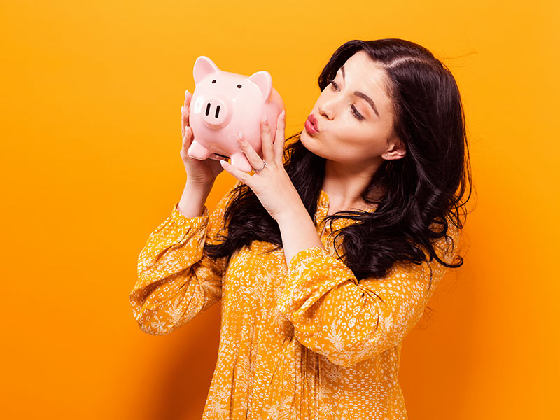 mulher em fundo amarelo segurando um porquinho pensando em abdominoplastia mamoplastia juntas preço