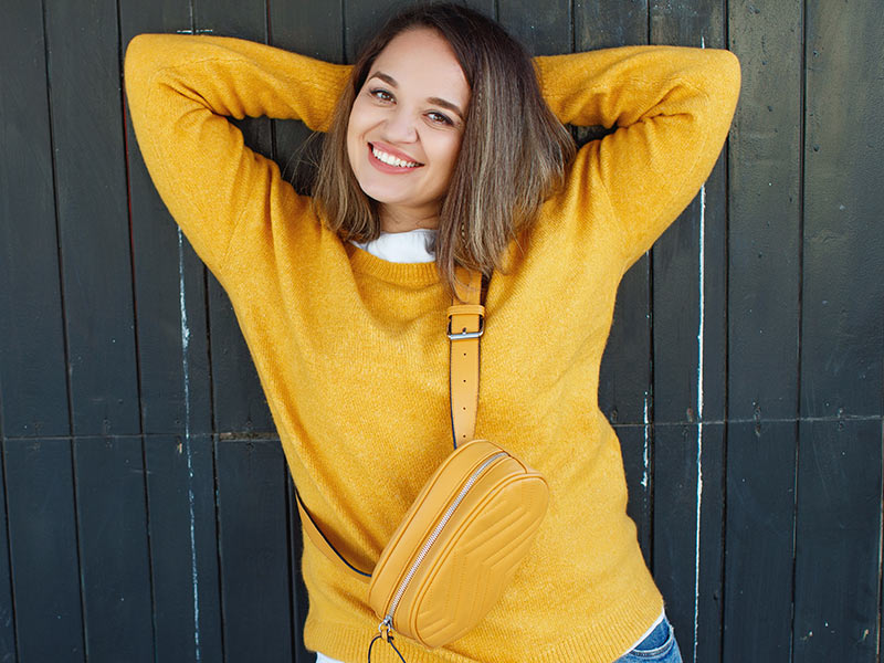 mulher feliz posando com roupa amarela levantando os braços após a lipo no braço