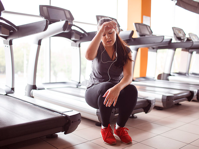 Mulher sentada na esteira cansada, depois de fazer exercício, como protocolo pós criolipólise