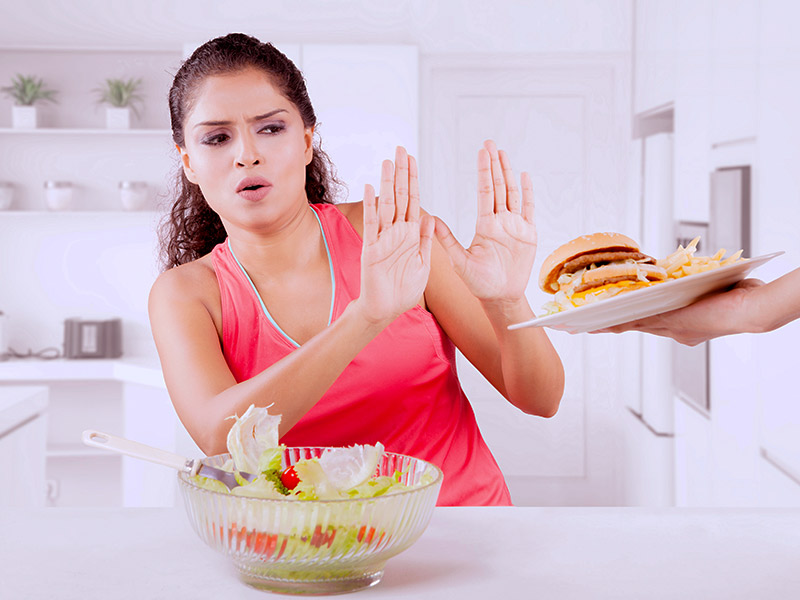 Mulher recusando um hambúrguer com batatas, que não pode comer depois da criolipólise