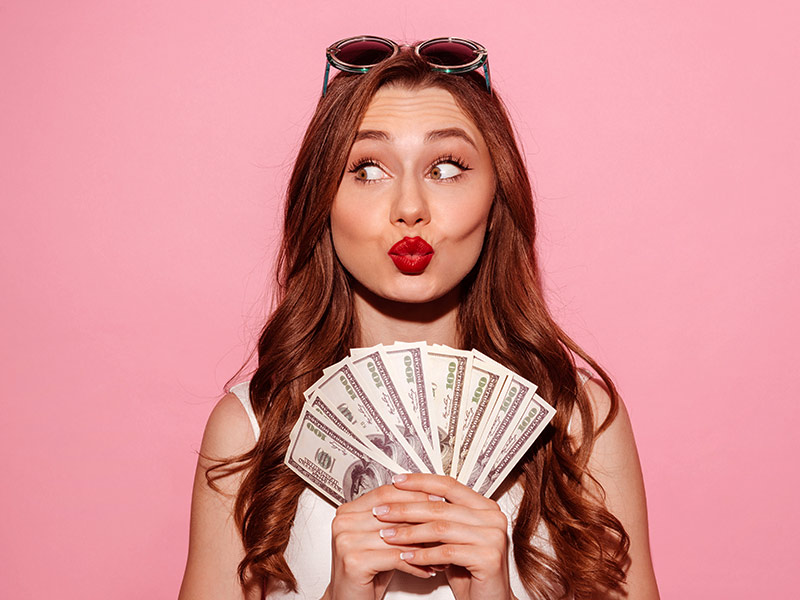 mulher em fundo rosa segurando notas de dinheiro feliz com o valor da lipo laser