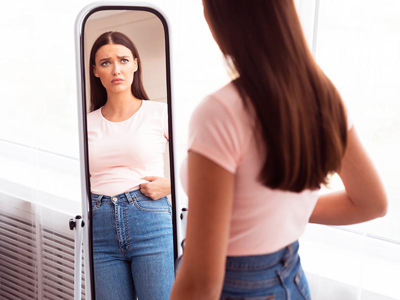 Mulher de camiseta rosa se olhando no espelho, avaliando o antes e depois da endermoterapia 