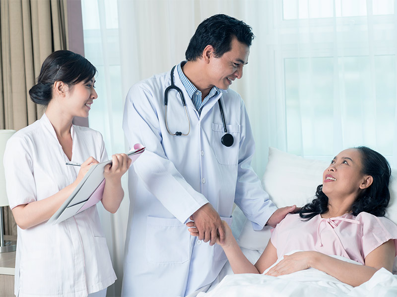 Médico e enfermeira explicando para paciente deitada na maca como é feita a Mamoplastia