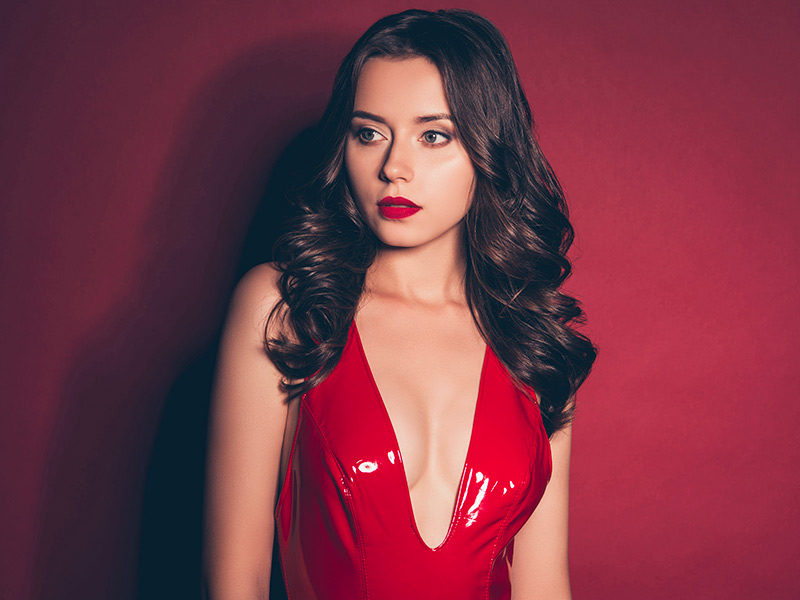 Mastopexia sem prótese de silicone Mulher morena de vestido vermelho bem decotado, após fazer a mastopexia sem prótese