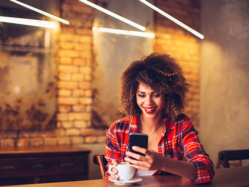 Mulher na cafeteria, pesquisando no celular o preço da areoloplastia 