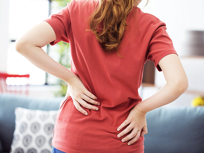 Mulher de camiseta vermelha com as mãos nas costas com dor, por causa da hipertrofia mamária
