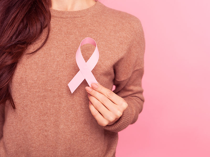 Mulher segurando um lacinho rosa na frente dos seios, representando a Mamoplastia Reparadora pós mastectomia 