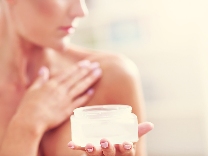 Como Diminuir os Seios? Mulher segurando um pote com a mão e a outra passando um creme para diminuir os seios