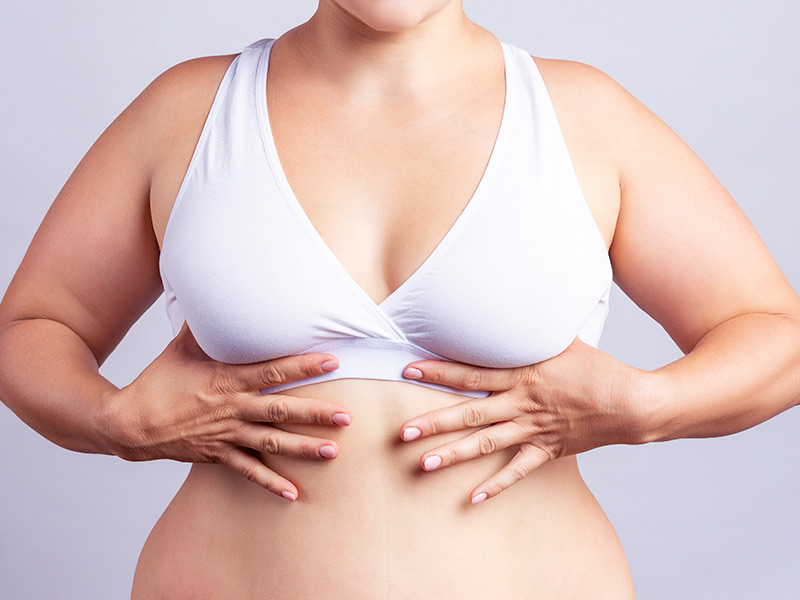 Como endurecer a mama? Mulher de top branco segurando a parte debaixo dos seios, pensando em como deixar os seios firmes
