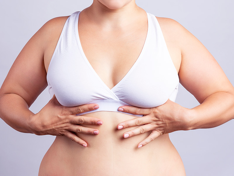 Mulher de top branco segurando a parte debaixo dos seios, pensando em como deixar os seios firmes