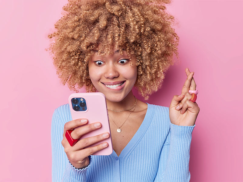 Mulher cruzando os dedos enquanto olha para o celular, torcendo pra ganhar a promoção de redução de seios