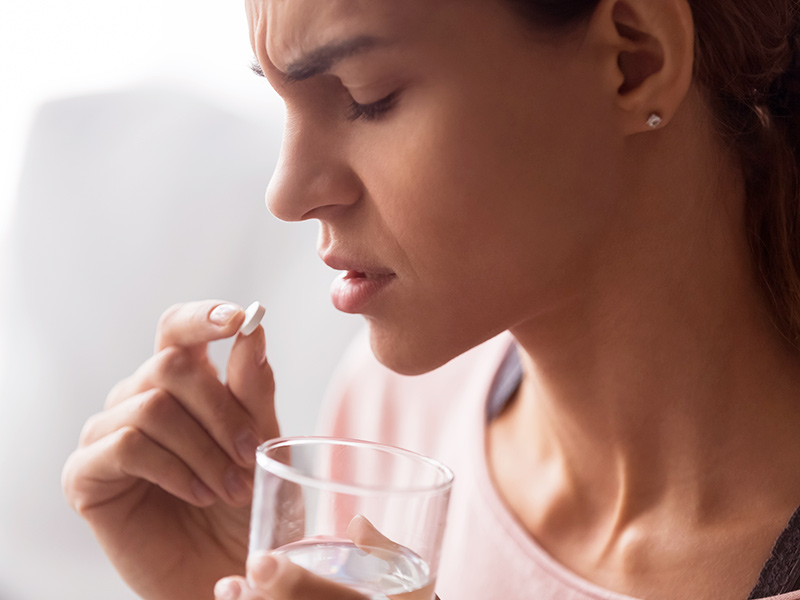 mulher tomando uma pílula de corticoide como tratamento para contratura capsular