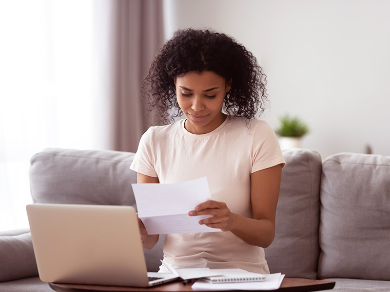 mulher sentada em frente a um notebook, ela está olhando um papel com as taxas hospitalares para colocar a prótese de silicone 