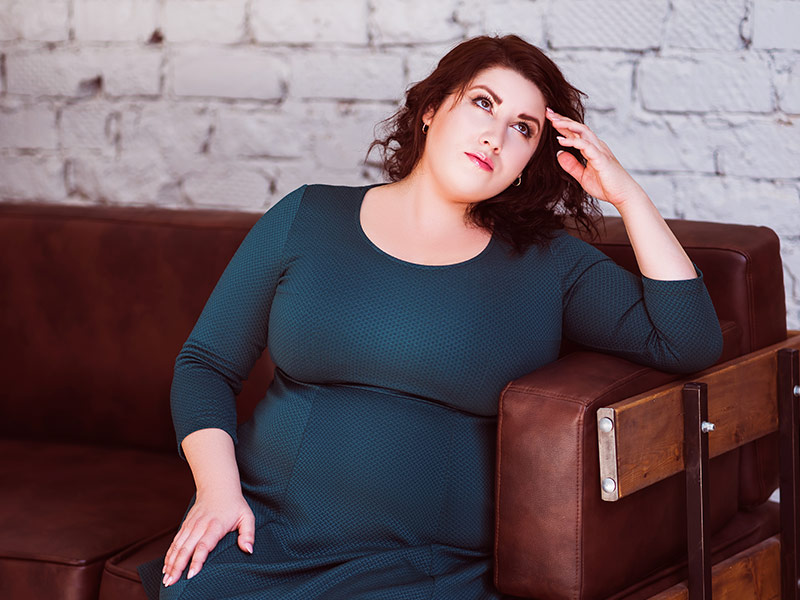 Mulher sentada no sofá, olhando para cima e pensando na recuperação após redução de mama