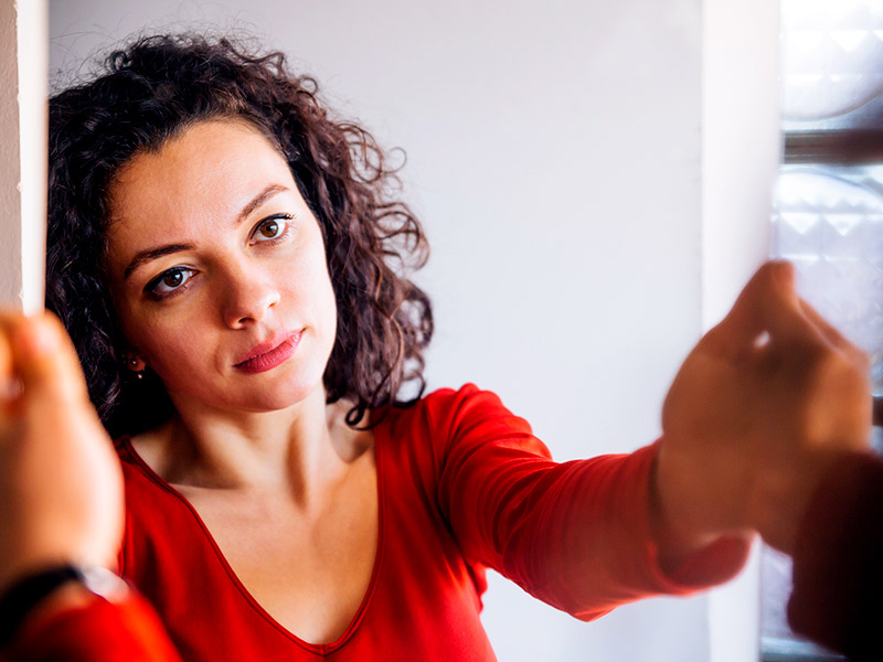 Imagem de uma mulher se olhando no espelho, observando o tamanho da asa nariz com uma expressão facial séria