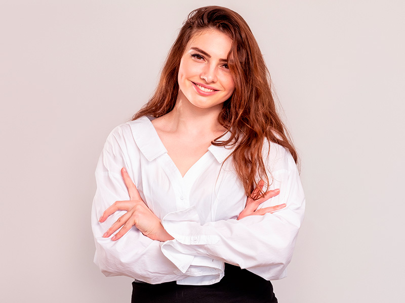 Mulher de camisa branca sorrindo com os braços cruzados