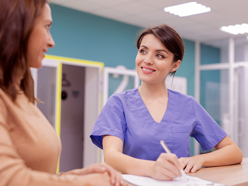 Imagem de uma enfermeira sorrindo para a paciente sendo atendida no retorno de pós-operatório