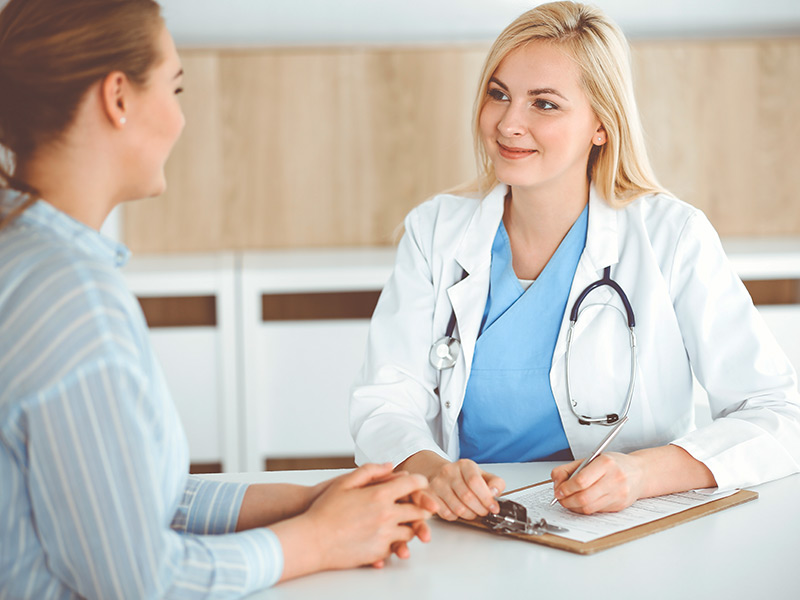 Médica com uma prancheta conversando com a paciente sobre a recuperação da rinoplastia