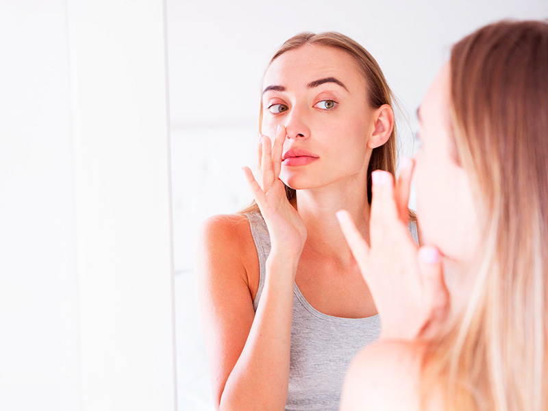 Mulher com a mão no nariz se olhando no espelho após usar o modelador de nariz