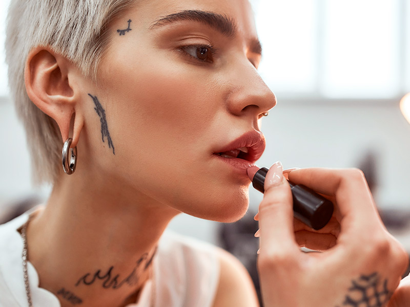 Conheça os tipos de otoplastia Imagem de uma mulher com o lóbulo da orelha rasgado passando batom