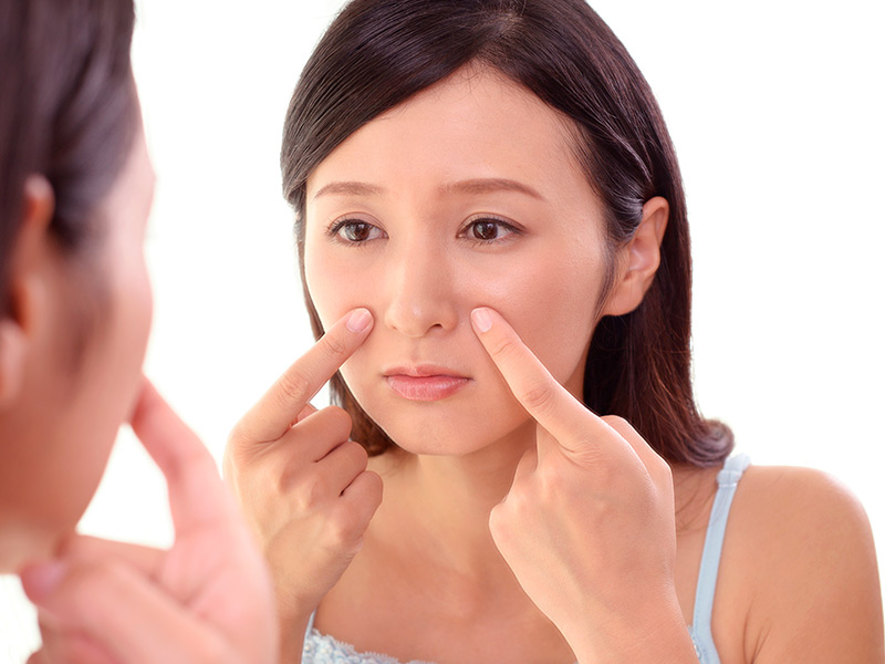 Imagem de uma mulher observando o nariz no espelho enquanto pensa sobre a rinoplastia gratuita