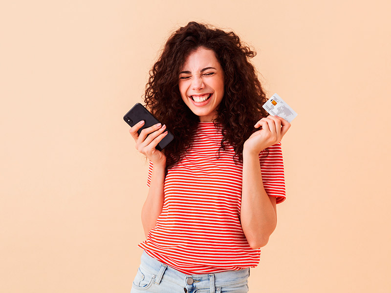 Mulher sorrindo de olhos fechados, segurando um cartão de crédito e celular, feliz com o preço da mamiloplastia, que serve para todos os tipos de mamilos