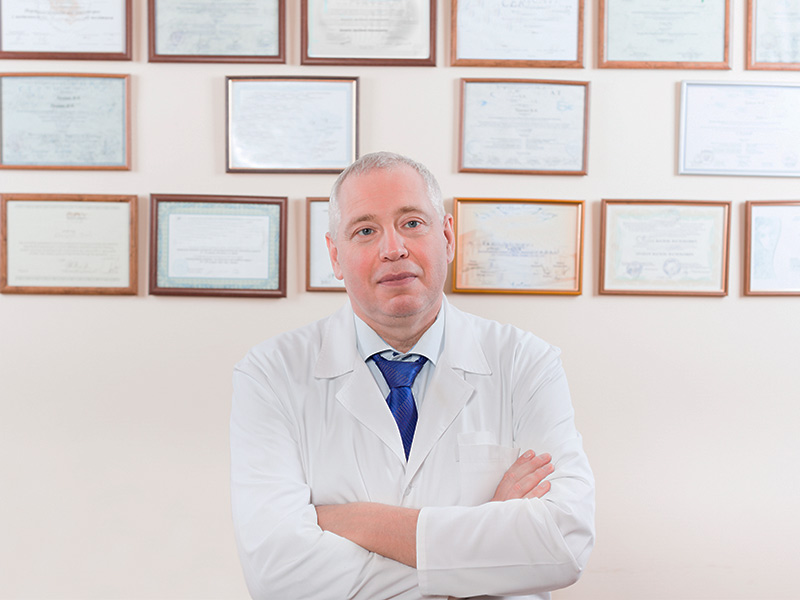 Conheça a equipe médica da clínica de cirurgia plástica Cirurgião experiente na clínica de cirurgia plástica posando em frente de seus diplomas