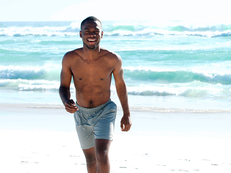 Homem de bermuda na praia, sorrindo feliz depois do tratamento da lipomastia 