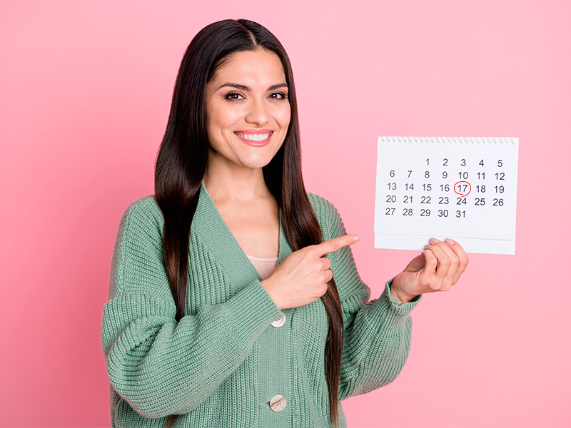 Mulher em um fundo rosa segurando um calendário com a marcação da data da sua consulta para cirurgia plástica